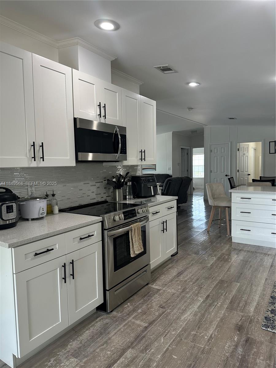 1570 Southwest 64th Way Boca Raton, FL 33428 - Photo 12 of 24 a kitchen with stainless steel appliances white cabinets a sink a stove a microwave and wooden floors