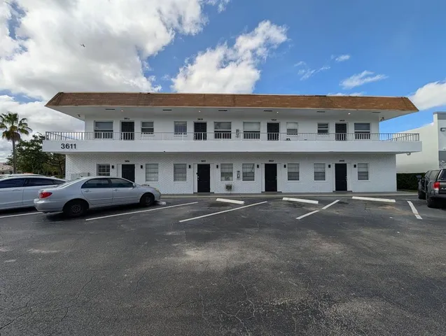 a front view of a building with lot of cars and trees