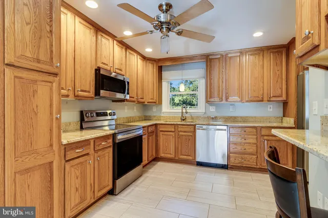 a kitchen with stainless steel appliances granite countertop a stove top oven a sink dishwasher and a refrigerator with wooden cabinets