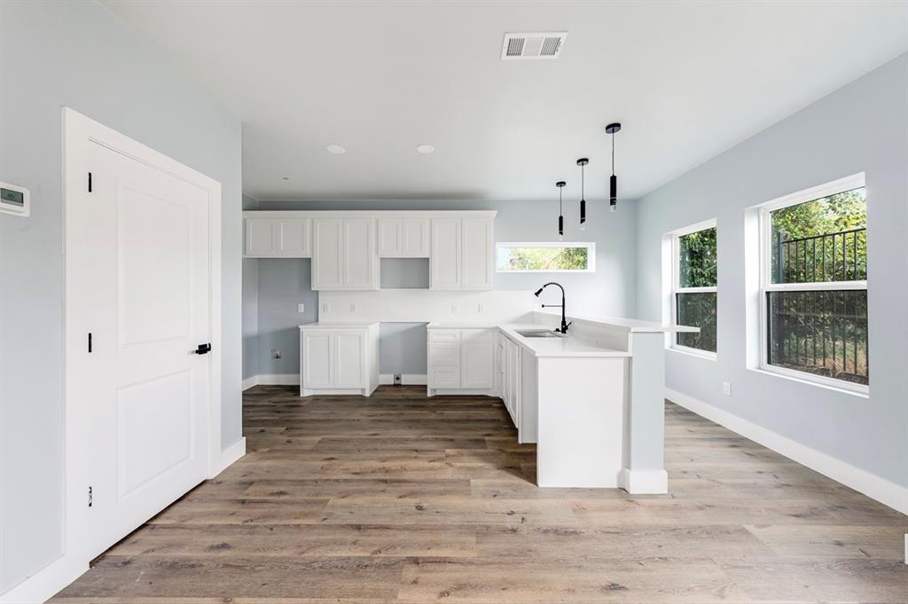 1113 East Oleander Street Fort Worth, TX 76104 - Photo 13 of 39 Kitchen featuring a peninsula, white cabinetry, light countertops, light wood-style flooring, and hanging light fixtures