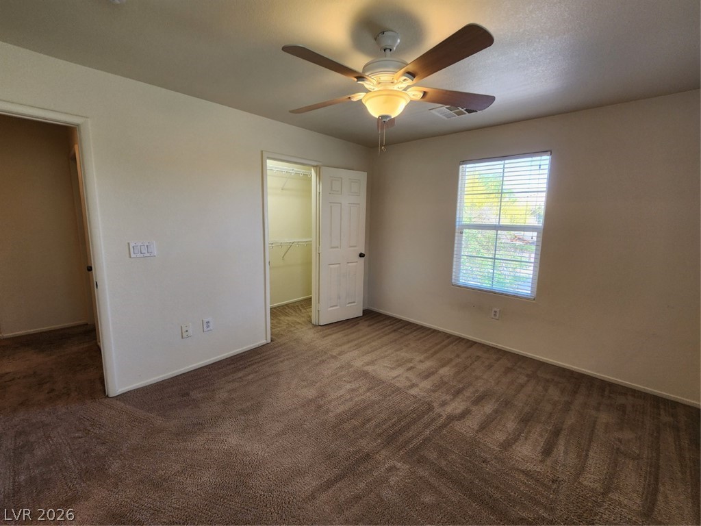 9132 Ripple Ridge Avenue, Unit 102 Las Vegas, NV 89149 - Photo 23 of 42 Unfurnished bedroom featuring a walk in closet, ceiling fan, and dark carpet