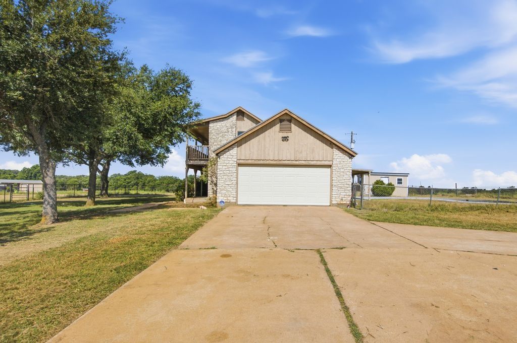 1454 Red Town Road Elgin, TX 78621 - Photo 23 of 40 A charming home with a garage and a balcony, nestled amidst a verdant landscape under a bright sky.