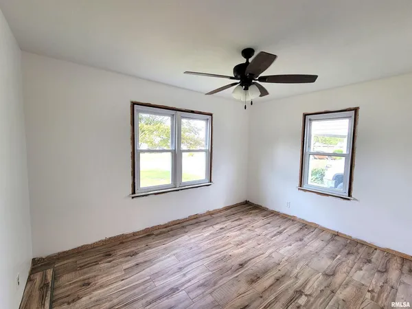 an empty room with wooden floor ceiling fan and windows