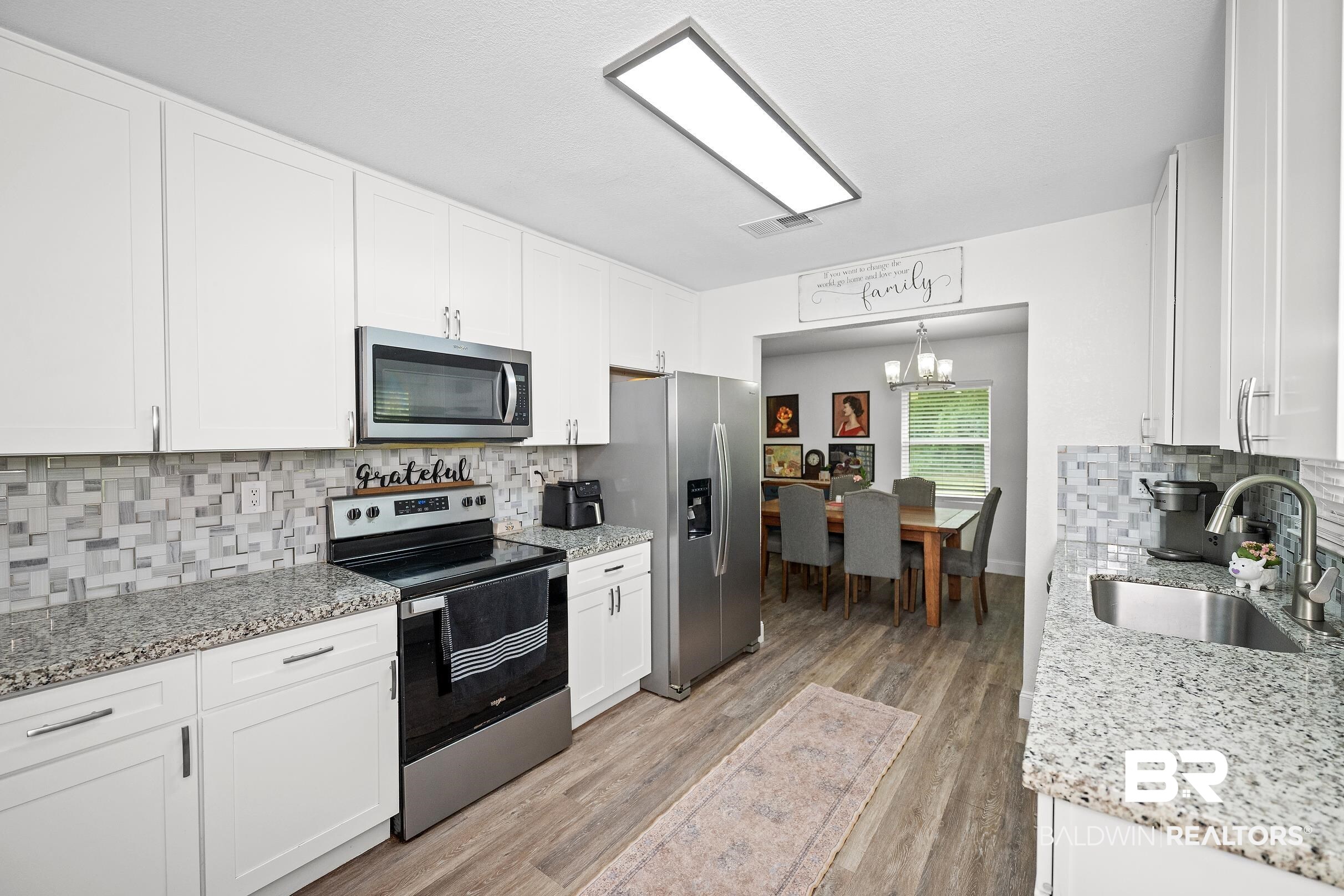 33129 Antietam Road Lillian, AL 36549 - Photo 5 of 31 Bright kitchen featuring white cabinetry, stainless steel appliances, speckled stone countertops, and a mosaic tile backsplash