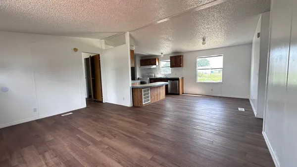 an empty room with wooden floor a kitchen view and a window