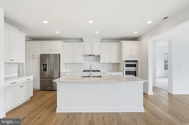 a large kitchen with kitchen island a sink a refrigerator and white cabinets