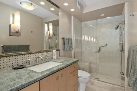 a bathroom with a granite countertop sink a toilet a mirror and shower