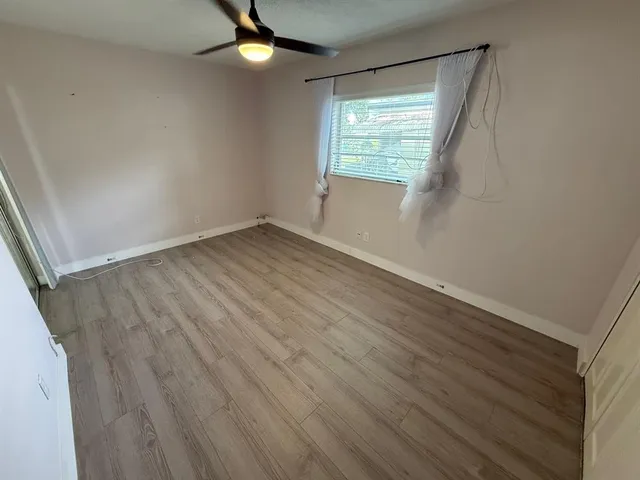 an empty room with wooden floor fan and windows
