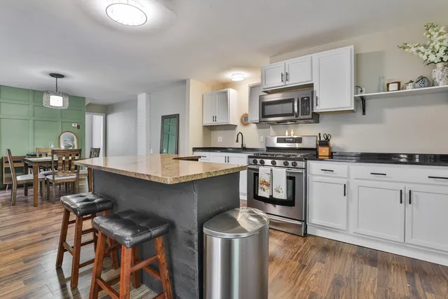 a kitchen with stainless steel appliances granite countertop a stove top oven a sink dishwasher and white cabinets with wooden floor