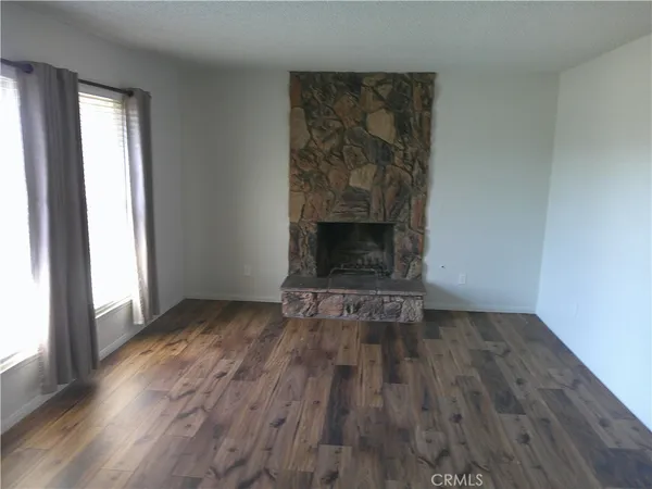 an empty room with wooden floor fireplace and windows