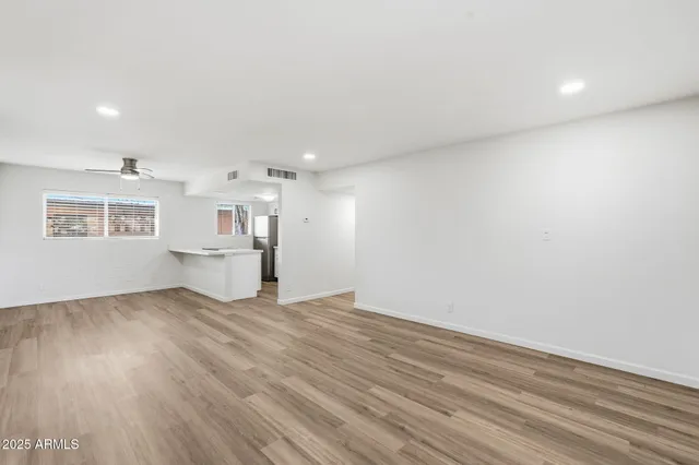 a view of empty room with wooden floor and kitchen