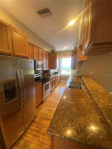 a kitchen with stainless steel appliances granite countertop a refrigerator a stove and a sink with wooden floor