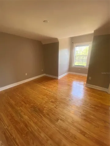 a view of an empty room with wooden floor and a window