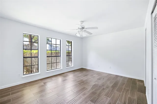 an empty room with wooden floor chandelier fan and windows