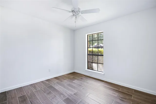 an empty room with wooden floor chandelier fan and windows