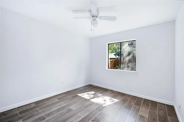 an empty room with wooden floor chandelier fan and windows