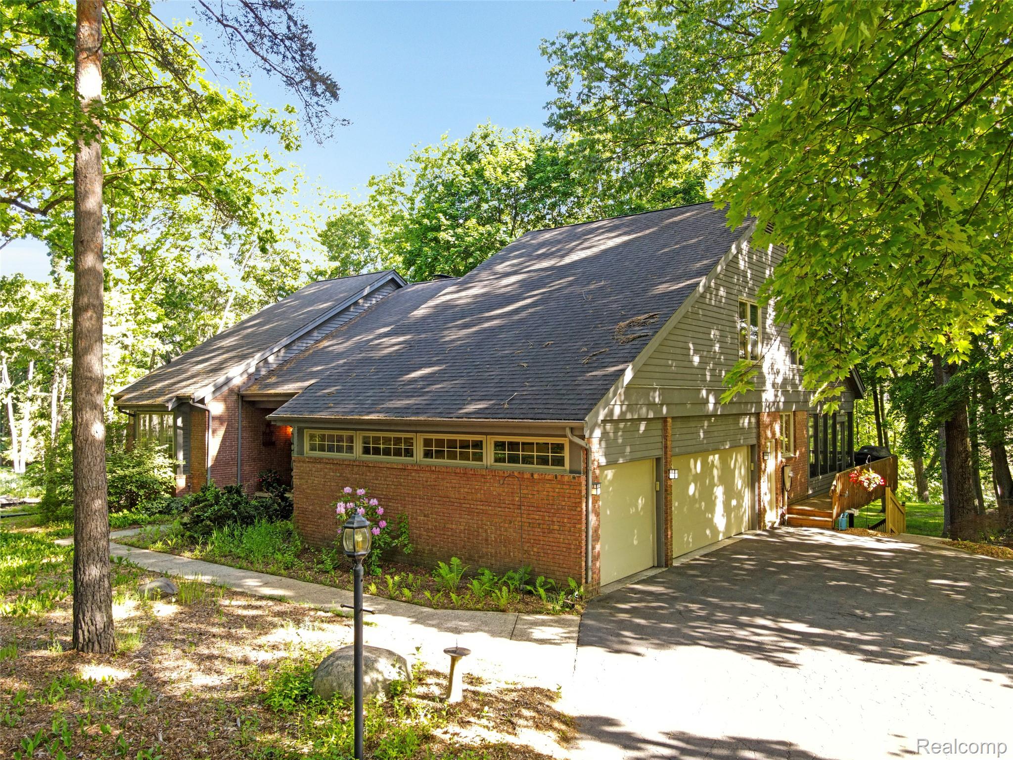 2323 Addaleen Road Highland, MI 48357 - Photo 18 of 70 Brick and siding exterior featuring a 3-car garage, multiple windows, and a shaded driveway