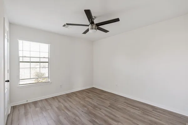 an empty room with wooden floor fan and windows