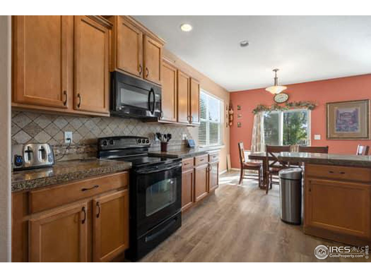 1545 Edenbridge Drive Windsor, CO 80550 - Photo 7 of 28 a kitchen with stainless steel appliances granite countertop a stove top oven a sink dishwasher a dining table and chairs with wooden floor