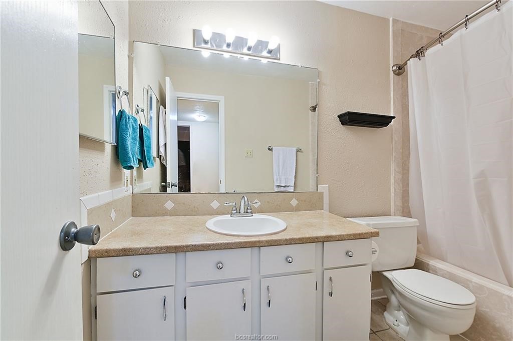 904 University Oaks Boulevard, Unit 155 College Station, TX 77840 - Photo 10 of 11 a bathroom with a granite countertop sink toilet a mirror a vanity and shower