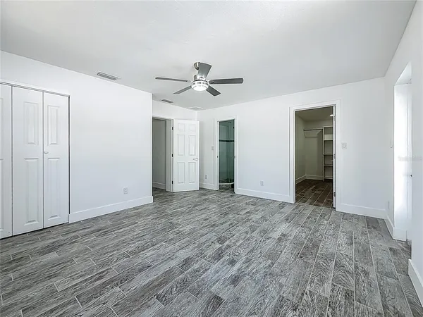 a view of an empty room with chandelier fan and wooden floor