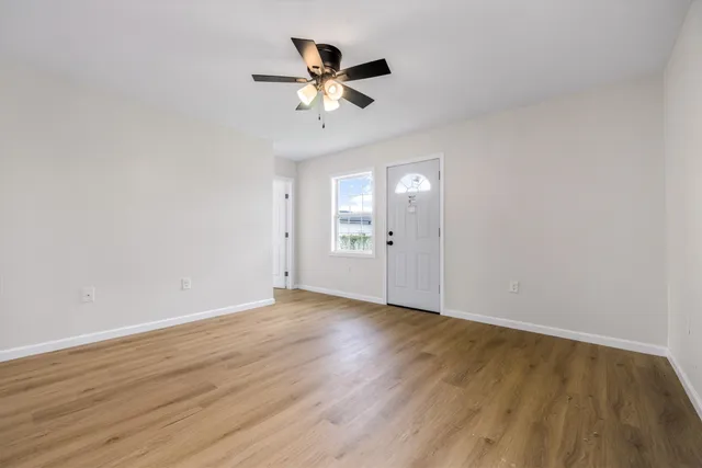 a view of an empty room with wooden floor and a ceiling fan