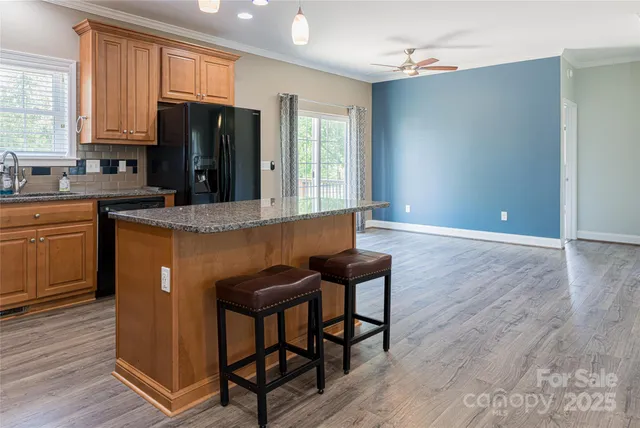 a kitchen with stainless steel appliances granite countertop a refrigerator a sink a stove a dining table and chairs with wooden floor