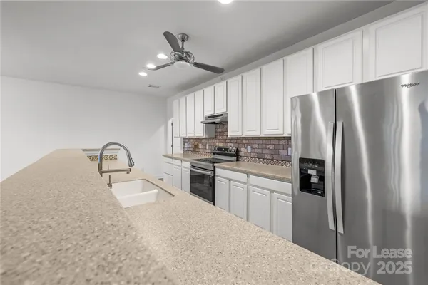 a kitchen with stainless steel appliances granite countertop a refrigerator a stove a sink and white cabinets