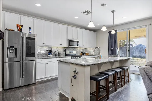 a kitchen with stainless steel appliances granite countertop a sink a stove a refrigerator cabinets and a dining table with wooden floor