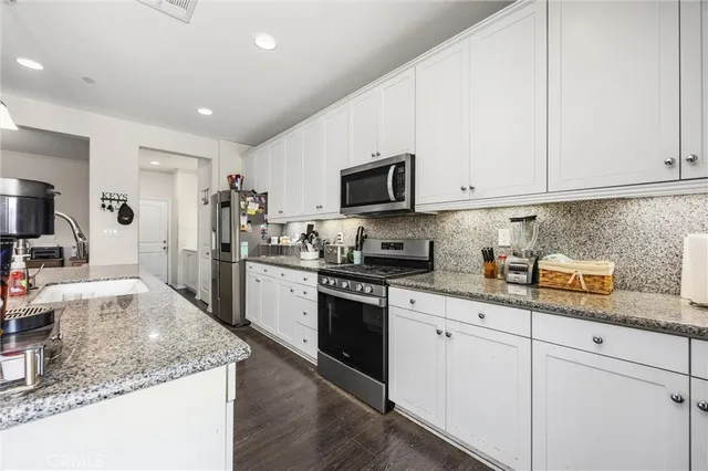 a kitchen with granite countertop a sink a stove top oven and white cabinets