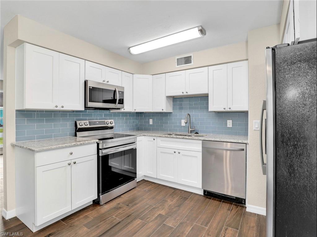 3 Knights Bridge Road, Unit A2 Naples, FL 34112 - Photo 3 of 19 Kitchen featuring dark wood-style flooring, stainless steel appliances, backsplash, a sink, and visible vents