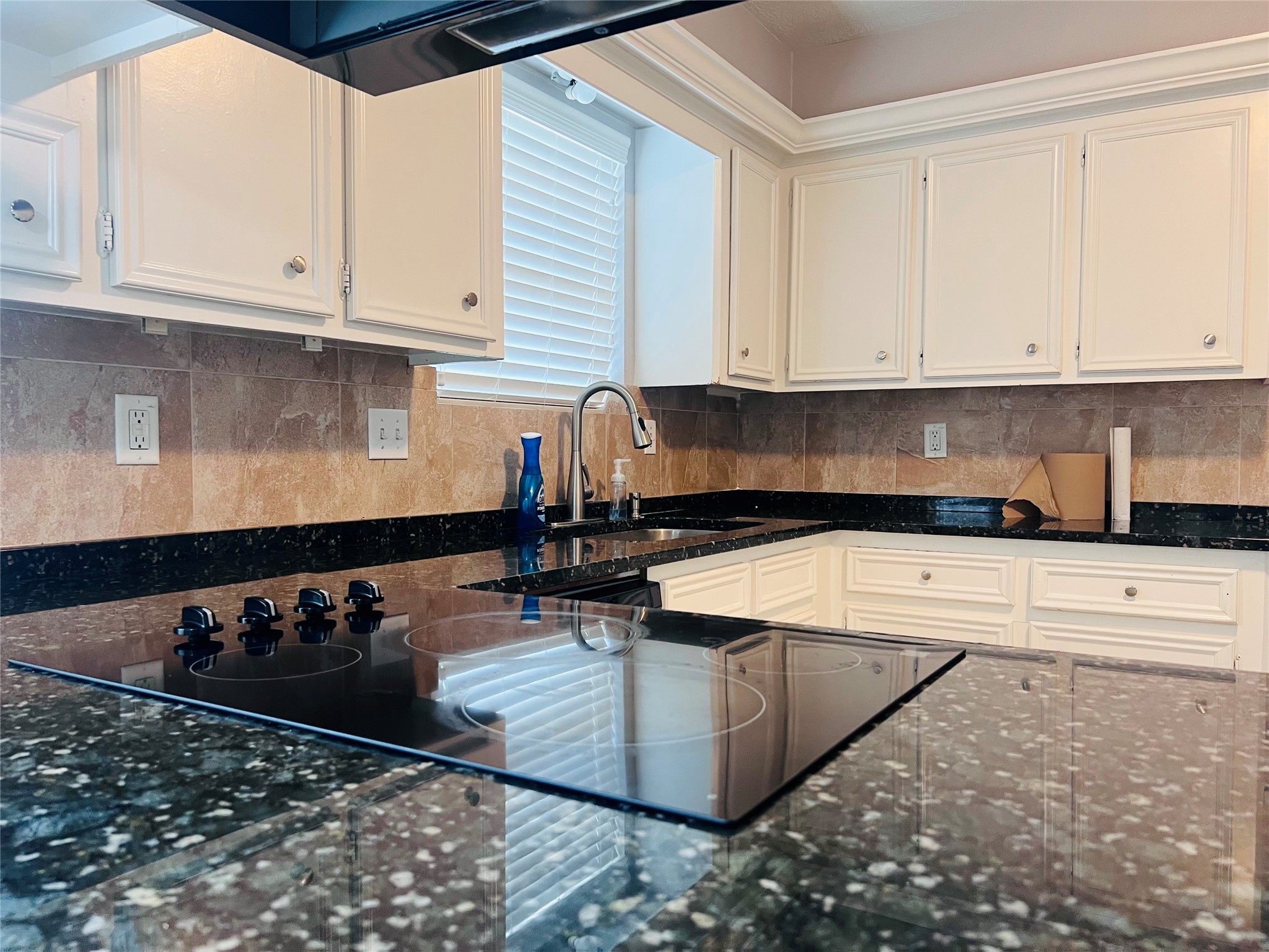 902 Hidden Canyon Road Katy, TX 77450 - Photo 6 of 20 Modern kitchen with granite countertops, sleek black cooktop, and white cabinetry. It features a double sink under a large window, providing ample natural light.