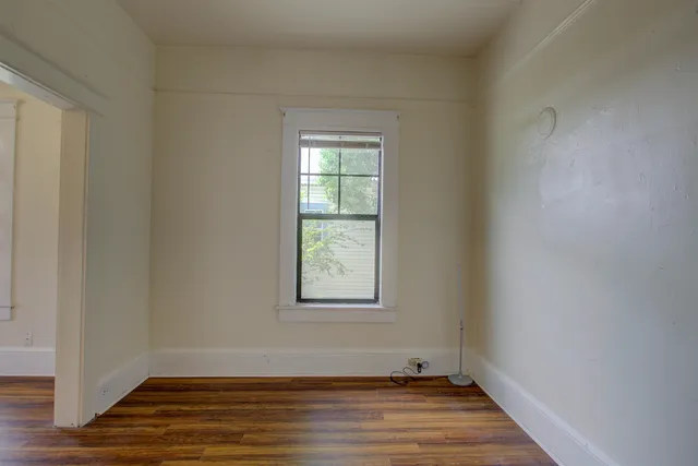 a view of an empty room with wooden floor and a window