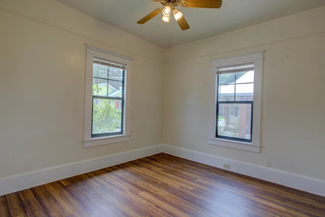 an empty room with wooden floor chandelier and windows