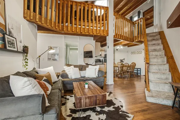a living room with couches a fireplace and kitchen view with wooden floor
