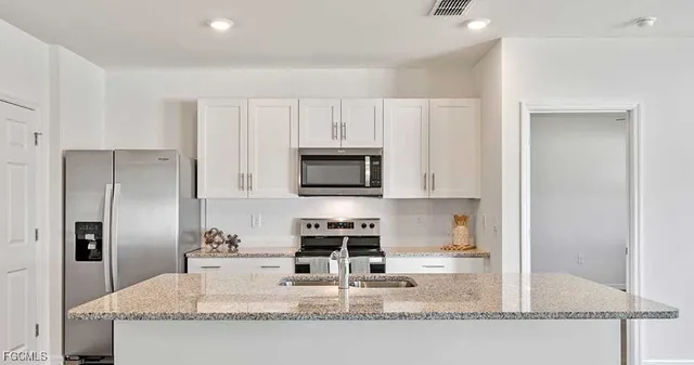 a kitchen with granite countertop a refrigerator a stove and white cabinets
