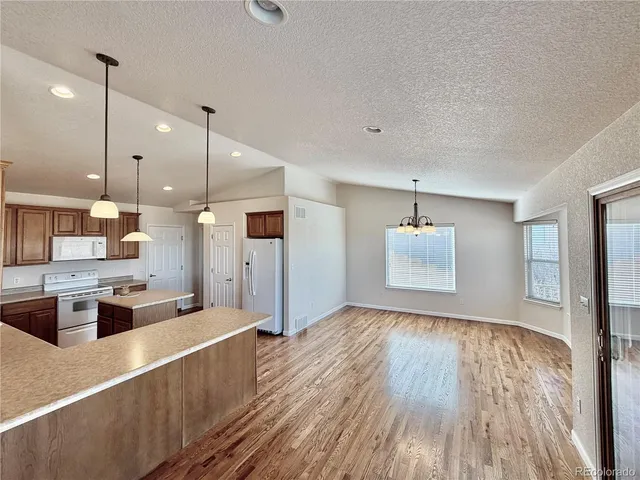 a large kitchen with kitchen island a stove a sink a refrigerator and white cabinets with wooden floor