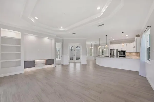a view of an empty room and kitchen view with wooden floor