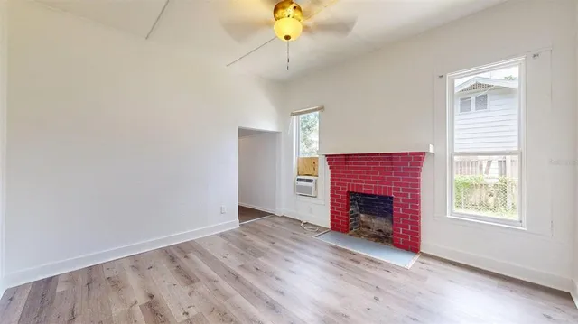 a view of an empty room with wooden floor fireplace and a window