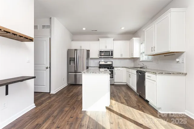 a kitchen with kitchen island a refrigerator a stove a sink and white cabinets with wooden floor