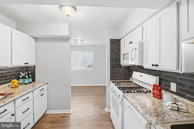 a kitchen with granite countertop a stove a sink dishwasher and white cabinets with wooden floor