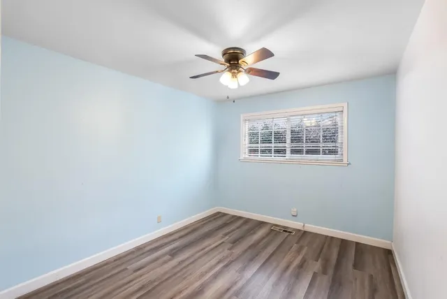 an empty room with wooden floor fan and windows