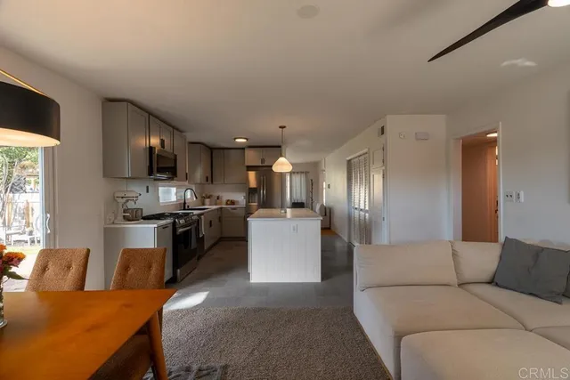 a living room with stainless steel appliances furniture a kitchen view and a refrigerator