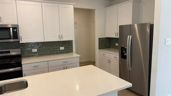 a kitchen with stainless steel appliances a refrigerator a stove a sink and white cabinets