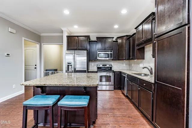 a kitchen with stainless steel appliances granite countertop a stove top oven a sink dishwasher a dining table and chairs with wooden floor