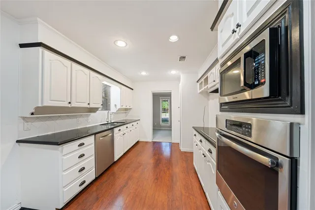 a kitchen with stainless steel appliances granite countertop a lot of cabinets and wooden floor