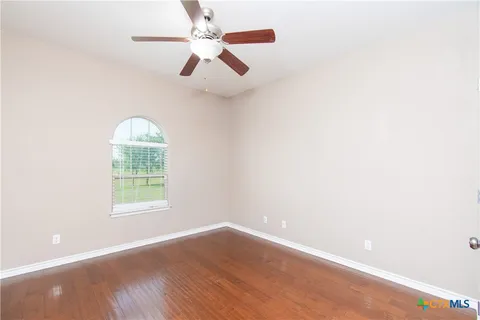 an empty room with wooden floor fan and windows