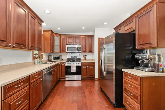 a kitchen with stainless steel appliances granite countertop wooden cabinets a refrigerator a sink a stove a microwave and wooden floors