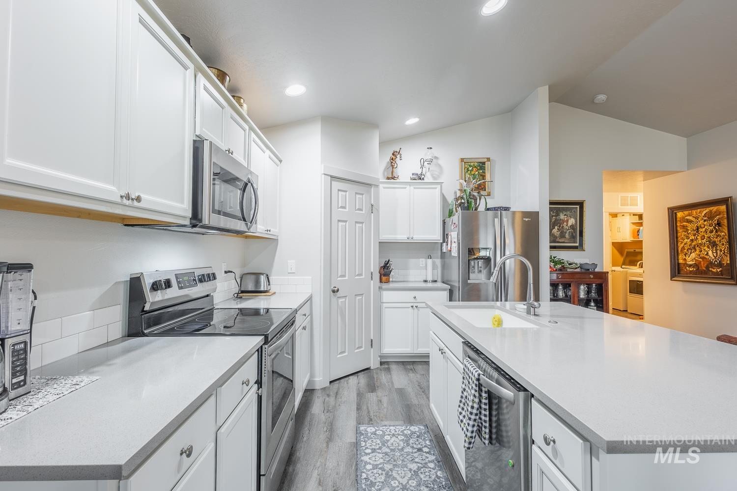 11309 West Viola Street Nampa, ID 83651 - Photo 19 of 37 Kitchen featuring appliances with stainless steel finishes, white cabinetry, light wood-style flooring, a center island with sink, and light stone counters