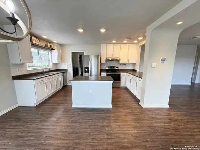 a large kitchen with stainless steel appliances granite countertop a large center island a stove a refrigerator white cabinets and wooden floor